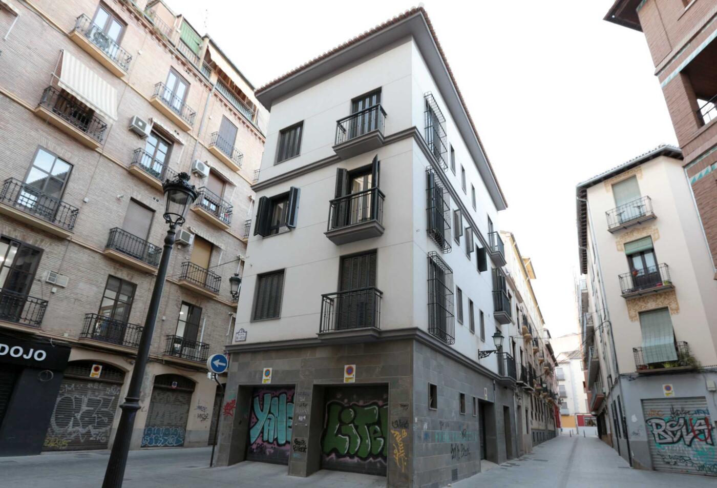 Esquina del edificio del apartamento Laurel, en una calle estrecha del centro de Granada: a pie de calle, dos puertas de garaje con sus placas de vado y, enfrente, una señal de dirección obligatoria.